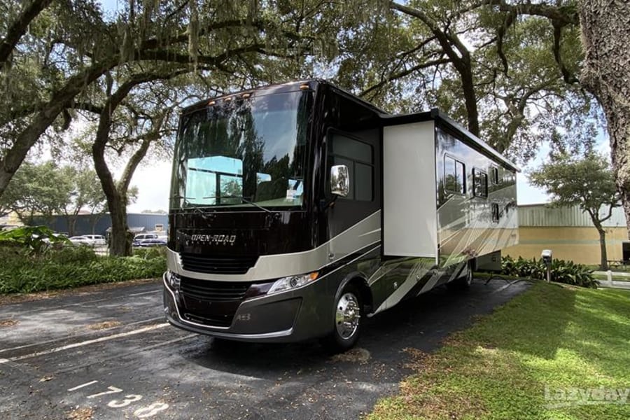 A dark Open Road RV rental with slide-out extended, parked under moss-draped trees. Perfect for spacious travels.
