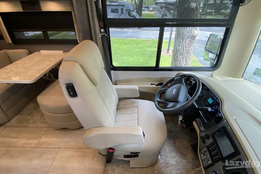 Inside an RV rental: view of driver's seat, dashboard, and the cozy living area with a table.