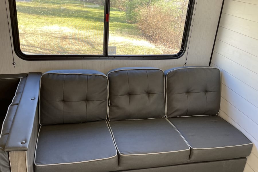 Cozy RV rental interior: A comfortable gray couch by a window overlooking greenery. Ideal for your next RV adventure.