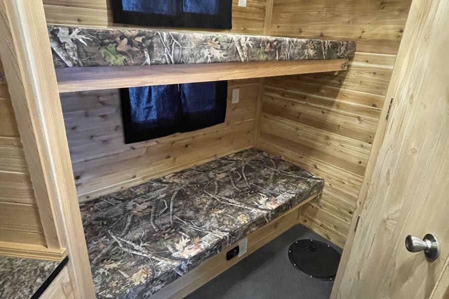 This RV rental ice fishing cabin interior features wooden walls, cozy bunk beds, and floor fishing holes.