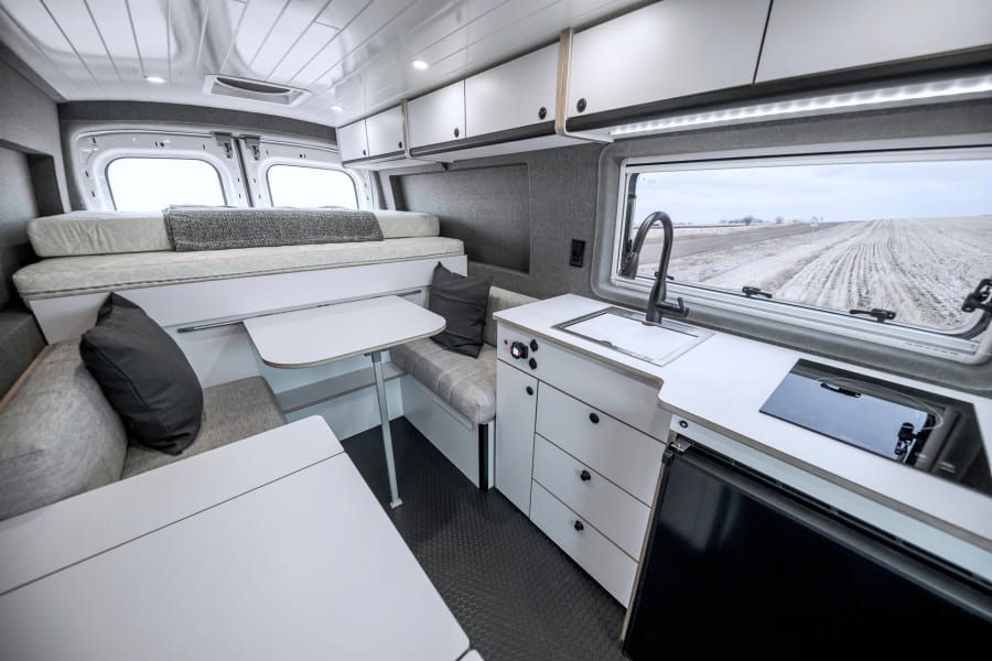 Spacious, modern RV rental interior featuring a cozy bed, dining area, and full kitchen, perfect for road trips.