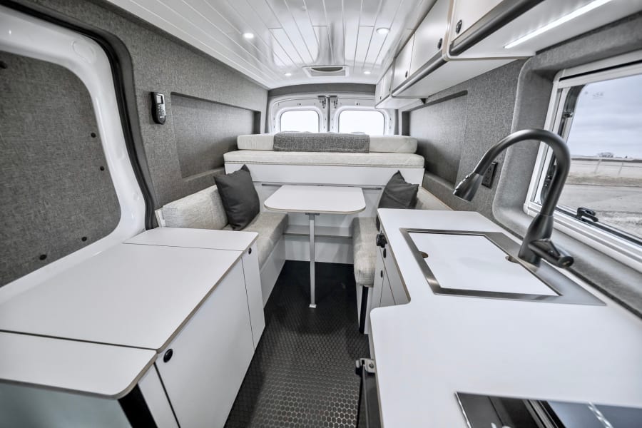 Explore a sleek rv rental camper van interior. White counters, gray walls, bed, kitchen, and dining for your adventures.