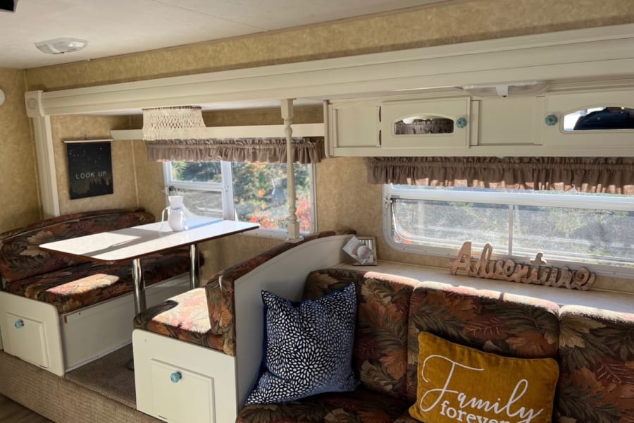 Cozy RV rental interior featuring a floral dining booth, comfortable seating, and bright windows, ideal for travel adventures.