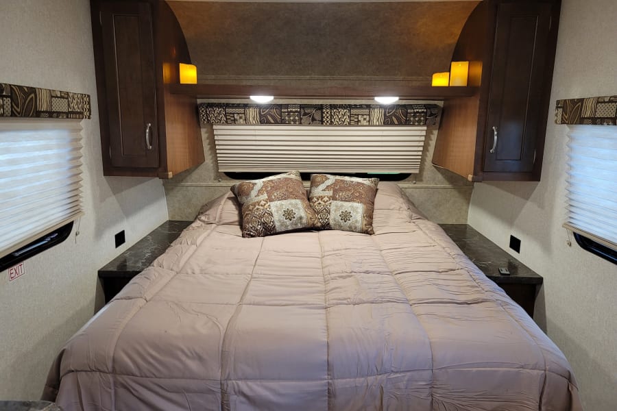 Cozy RV rental bedroom with a comfy bed, patterned pillows, overhead cabinets, and soft ambient lighting for a relaxing stay.