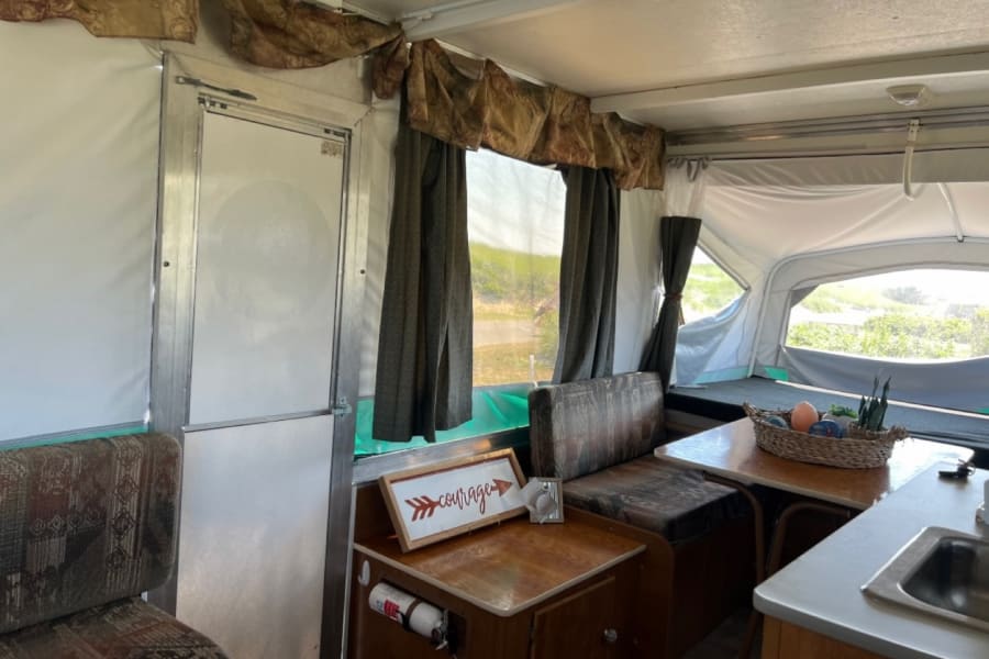 Cozy RV rental interior: view of dinette, kitchen sink, and windows with curtains in a compact pop-up camper.