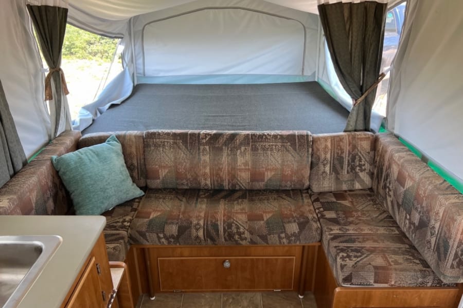 Cozy RV rental interior featuring a patterned dinette, a large bed area, and a compact sink. Ready for adventure!