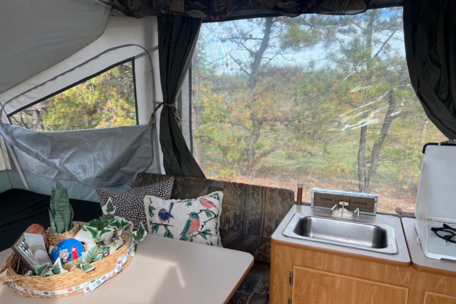 Cozy RV rental interior with dining, kitchen, and nature views through large windows, ideal for travel.