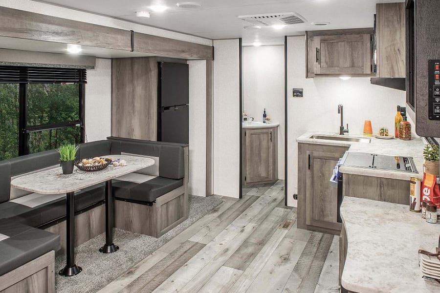 Spacious RV rental interior with a modern kitchen, dining booth, and light wood-look flooring.