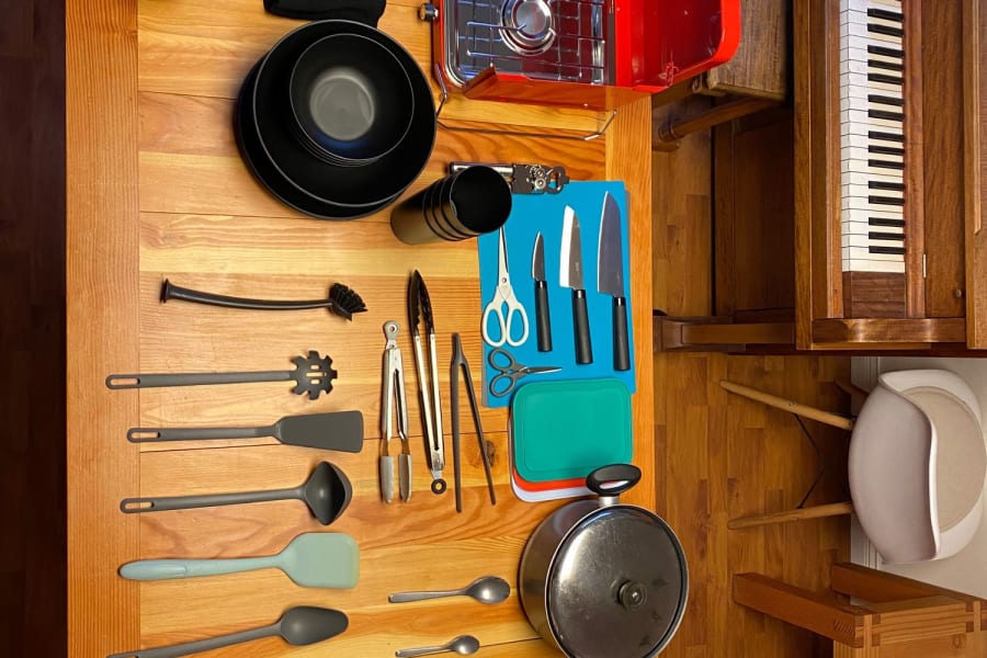 RV rental kitchen: portable stove, cooking utensils, black bowls, and pots/pans neatly arranged on a wood table.
