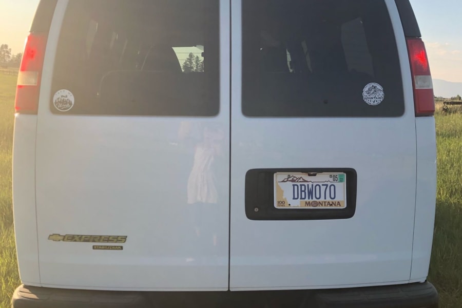 White Chevrolet Express van, an RV rental, parked in a sunny, grassy field under a clear sky, ready for adventure.
