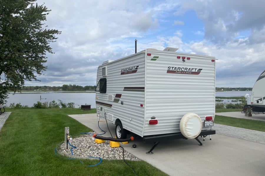 This rv rental is set up lakeside on a paved pad, complete with water, sewer, and power hookups, and a spare tire on back.