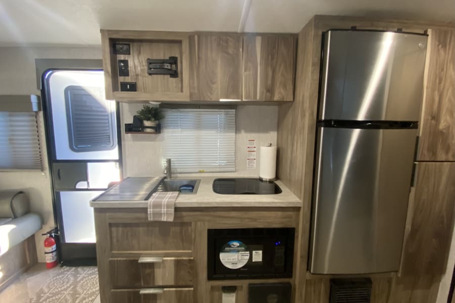 Kitchen area with single basin stainless steel sink, cook top, two drawers, microwave, and refrigerator.