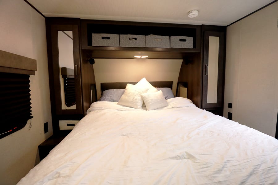 Spacious RV rental bedroom featuring a large bed with white linens, overhead storage, and mirrored cabinets for a comfortable stay.