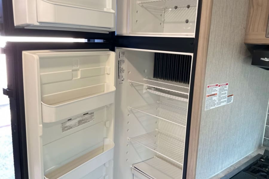 Explore this clean, empty RV rental refrigerator and freezer, ready for your adventures. Part of the kitchen's stove is visible too.