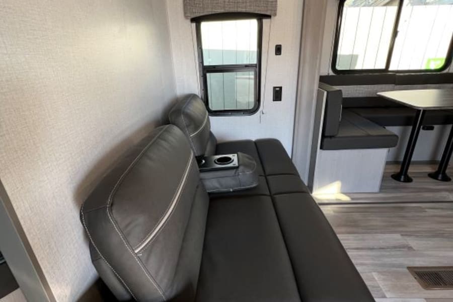 RV rental interior features a gray convertible sofa/bed, large windows, and overhead storage. Ideal for road trips.
