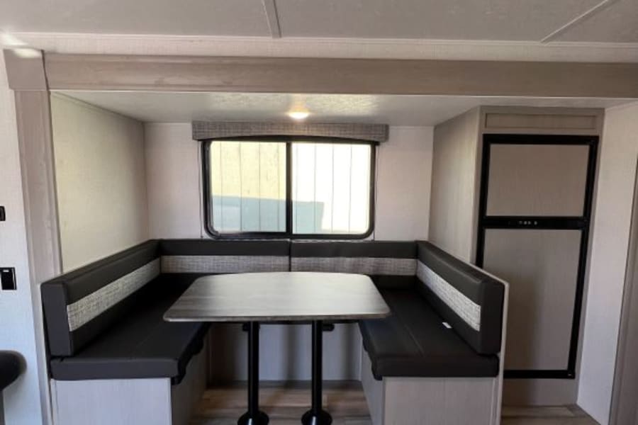 Experience your RV rental! Interior features a bright dinette with bench seating, table, and compact kitchen area. Note wood-look floor.