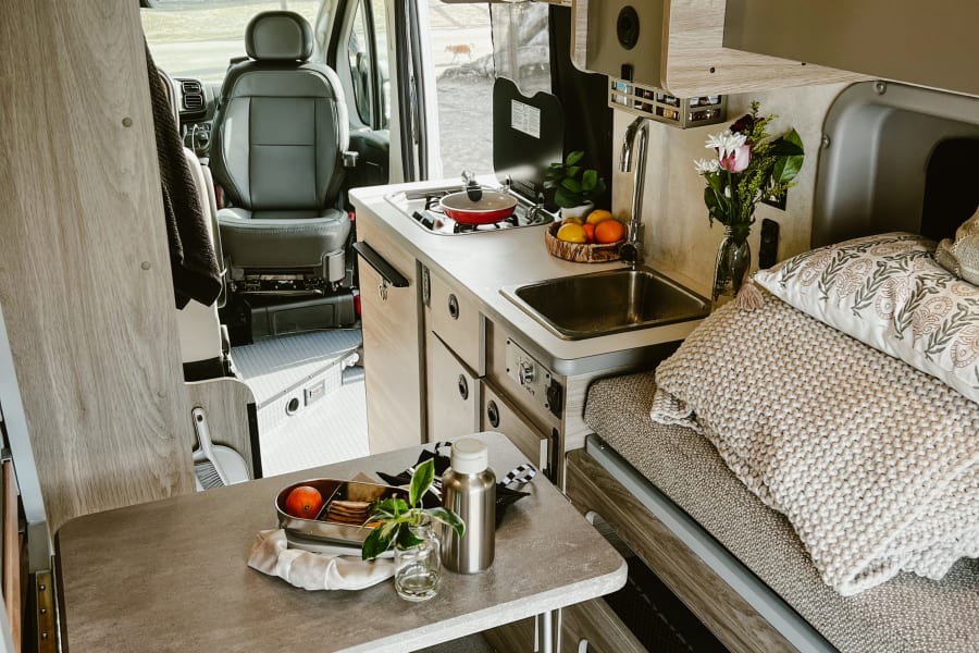 Inside a stylish RV rental, showcasing a fully equipped compact kitchen, dining area, and comfortable sleeping space.