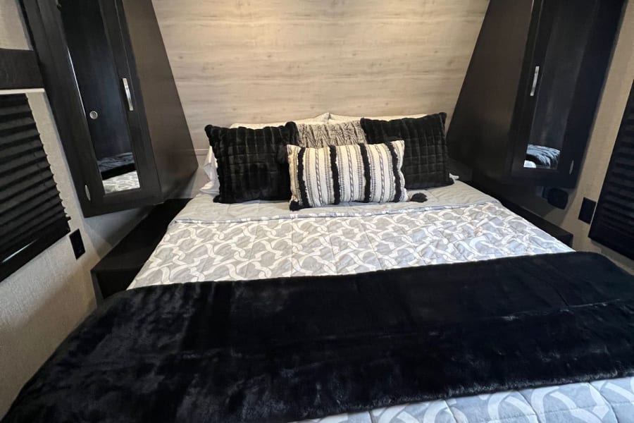 Cozy RV rental bedroom with patterned bedding, black throw, and compact overhead storage.