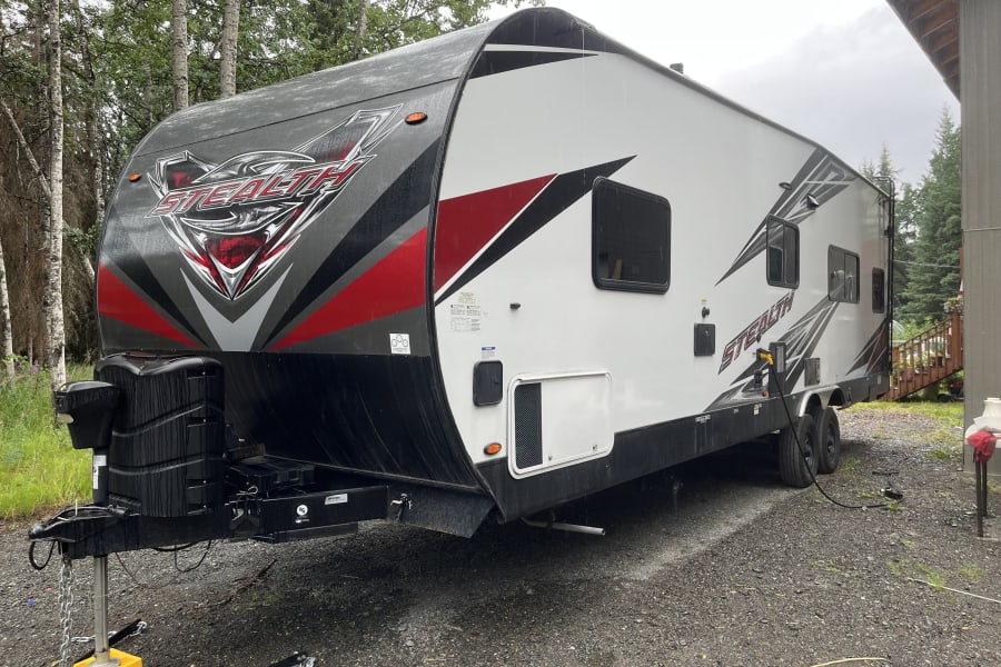 Stealth travel trailer RV rental: a large, modern recreational vehicle parked outdoors, showing wet surfaces.