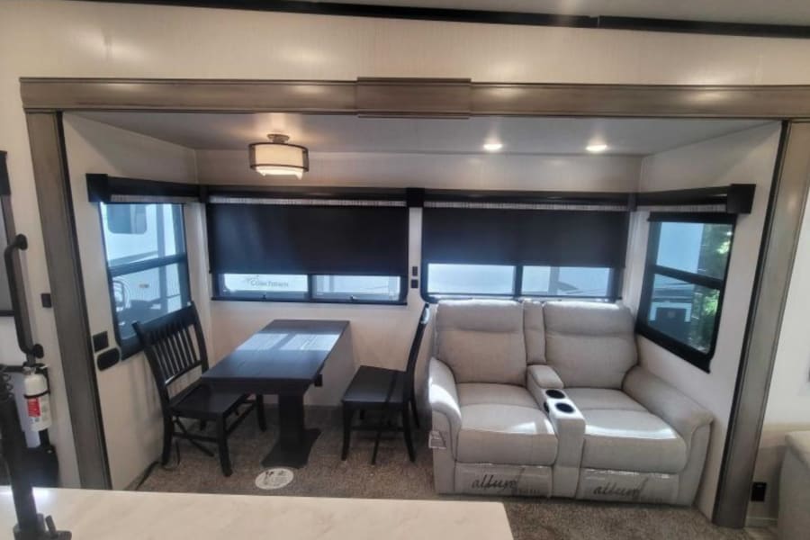 RV rental interior: cozy living space with a dining table, chairs, and comfortable recliners under large windows.