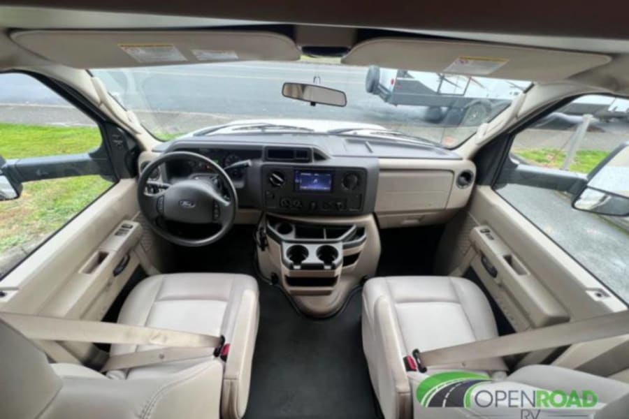 RV rental front cockpit view: driver and passenger seats, dashboard, steering wheel. Spacious interior setup.