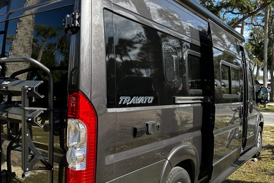 Dark grey Winnebago Travato rv rental. This camper van features an awning and rear rack, ideal for road trips.