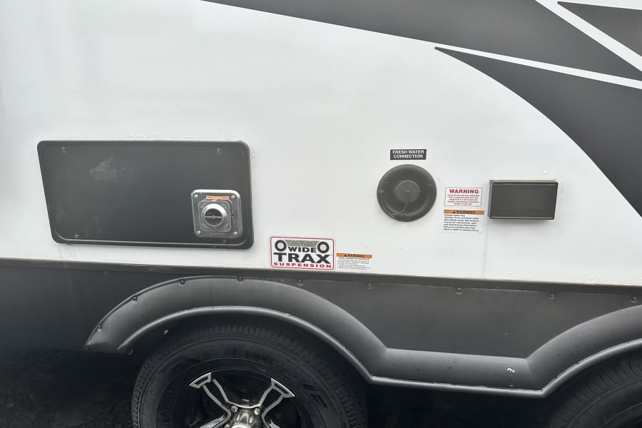 An RV rental's side shows a fresh water hookup, Dometic outdoor shower, and "Wide Trax Suspension" decal with warning labels.
