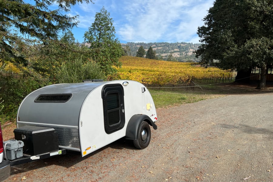 Scenic RV rental trip! A teardrop camper by a golden autumn vineyard, offering beautiful views of rolling hills under a blue sky.