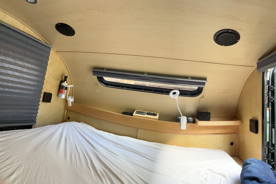 Cozy interior of an RV rental: features a comfortable bed, wooden walls & ceiling, and a window for travel.