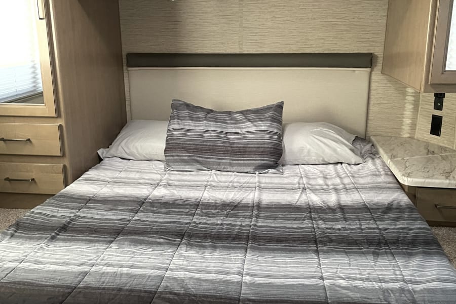 Cozy RV rental bedroom featuring a striped comforter, overhead cabinets, and compact built-in storage.