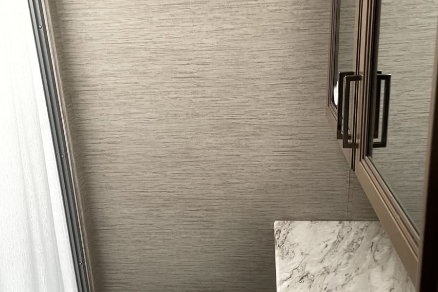 RV rental compact bathroom showing toilet, sink, vanity, mirrored cabinet, and shower. Light, textured walls.