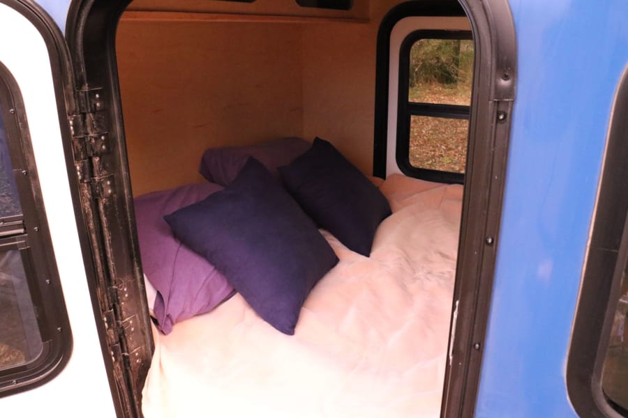 Cozy RV rental interior features a bed with pillows & a window view of fall foliage.