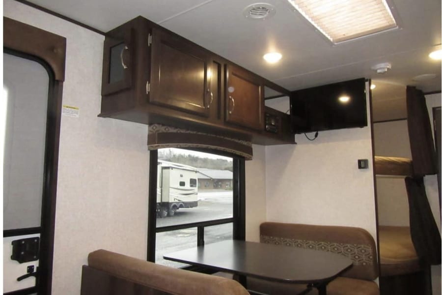 Explore this RV rental's living space: a dinette, wall-mounted TV, storage cabinets, and bunk beds.