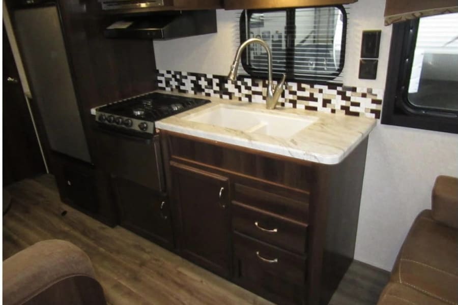 This RV rental's kitchen features a refrigerator, stovetop, double sink, and microwave above a stylish tiled backsplash.