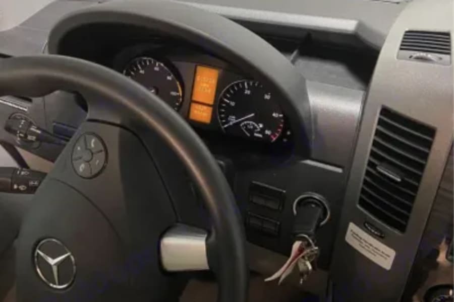 Driver's cockpit of a Mercedes-Benz Sprinter RV rental, showing the steering wheel, dashboard, and ignition keys.
