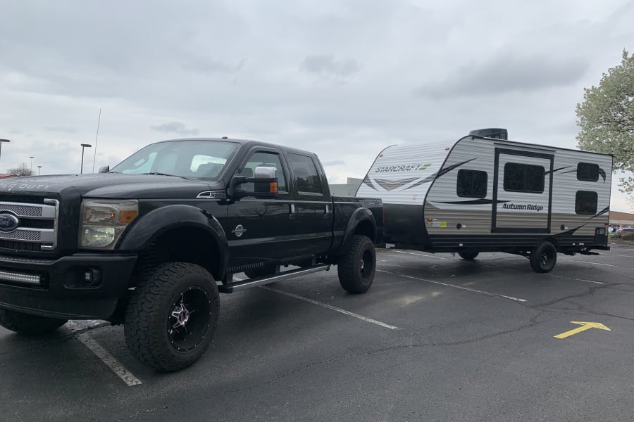 Black Ford F-350 truck towing a Starcraft Autumn Ridge travel trailer (RV rental) in a paved lot. Ready for adventure!