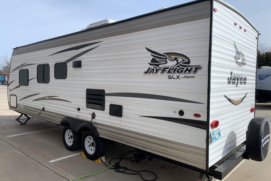 An Oklahoma-based Jayco travel trailer RV rental, equipped with hookups and leveling jacks, is parked.
