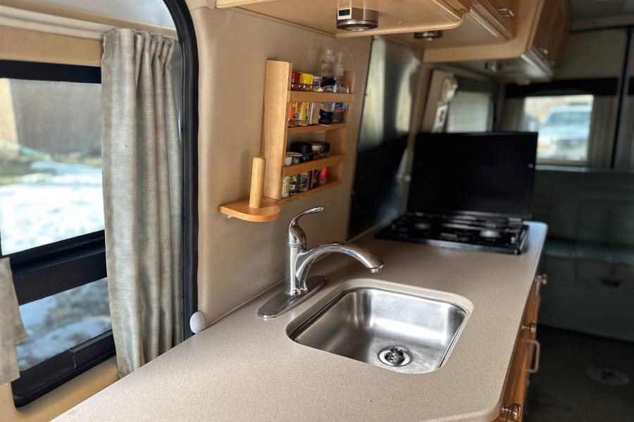 An RV rental's well-equipped kitchen with a stainless steel sink, chrome faucet, beige countertop, and handy spice rack.
