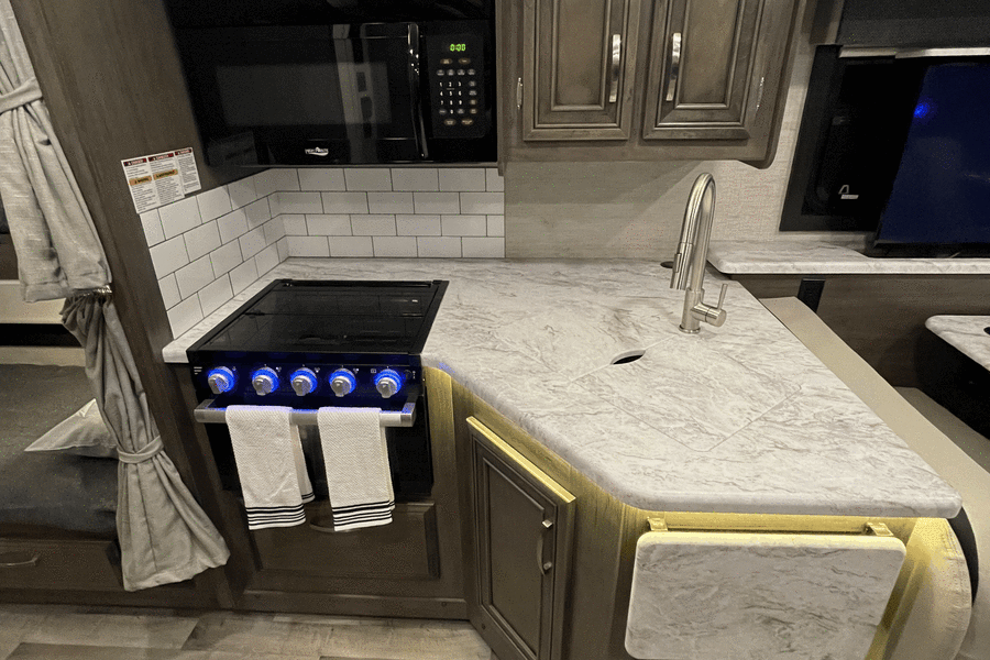 RV rental kitchen featuring a light grey countertop, dark cabinets, white subway tile backsplash, microwave, and stove.