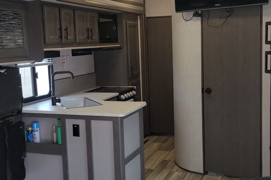 Spacious RV rental interior with a modern kitchen, living area, TV, and ceiling fan. Includes unique floor tie-downs.