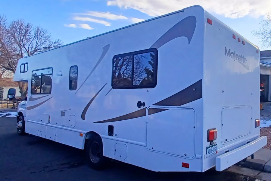White Majestic RV rental parked outdoors, showing its side profile with windows and brown decals under a blue sky.