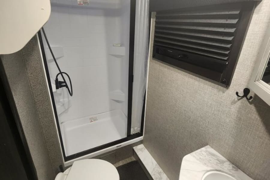 RV rental bathroom with a compact layout featuring a standing shower, toilet, and sink with a marble-look counter.