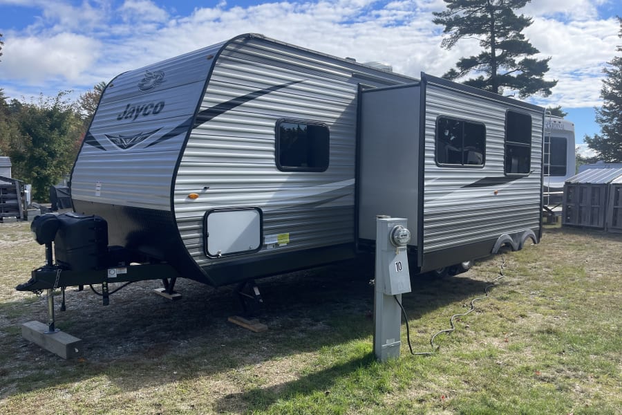 Explore outdoor adventures with this Jayco travel trailer, an ideal RV rental set up at a campsite with power hookup.