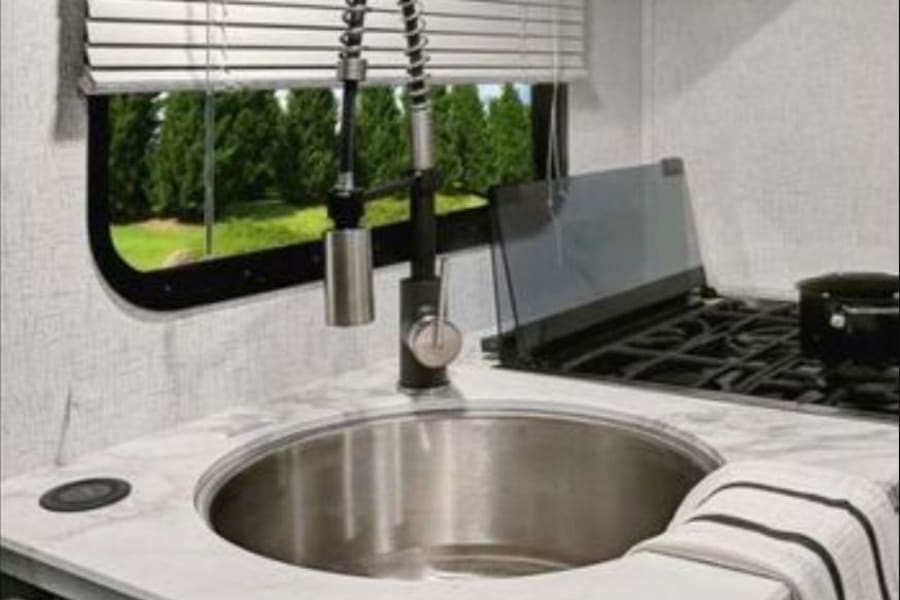 RV rental: Compact kitchen interior with a modern sink, spring-coil faucet, stove, and window view.