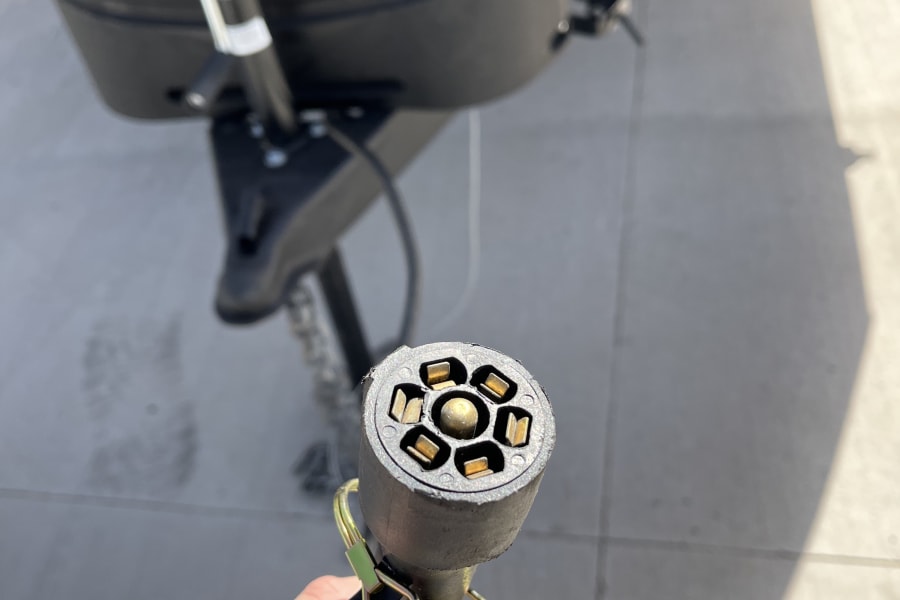 Closeup of a hand holding a 7-pin RV trailer electrical connector, essential for an RV rental hookup.