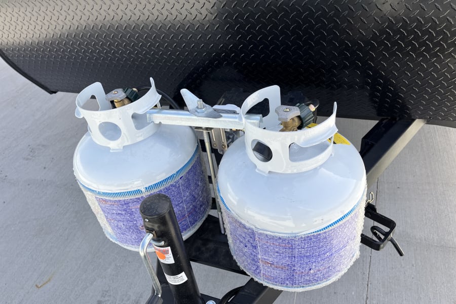 Dual white propane tanks on an RV rental trailer hitch, protected in bubble wrap, ready for your trip.