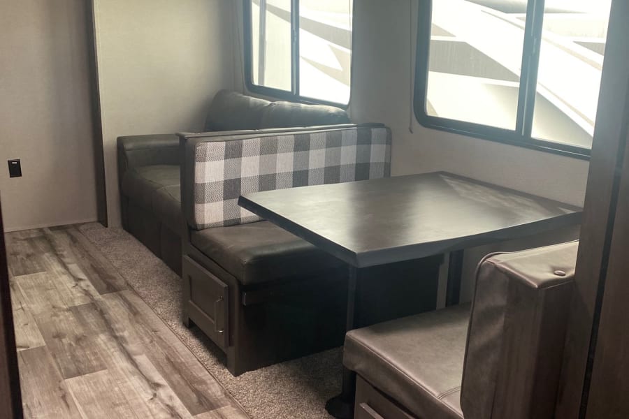 This RV rental offers a comfortable dinette with dark upholstered booth seating, a matching table, and large windows.