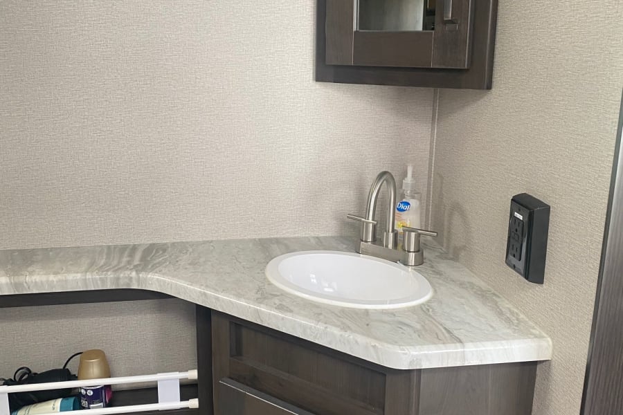 RV rental bathroom featuring a modern corner vanity with sink, mirrored cabinet, and convenient open shelving storage.