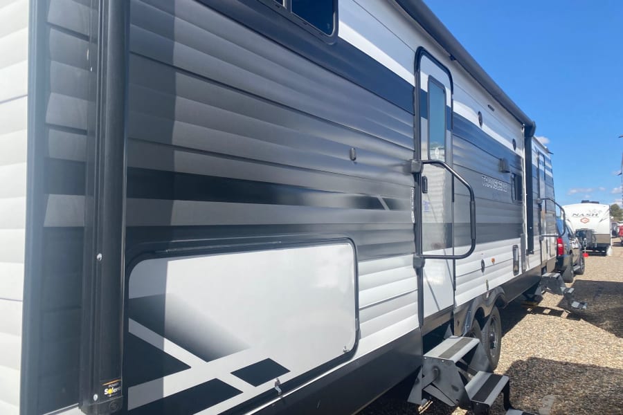 Exterior of a sleek black, white, and grey rv rental travel trailer, featuring entry steps and a storage compartment.