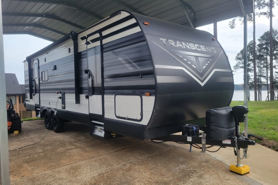 Transcend travel trailer RV rental, parked under a carport by a lake, ready for your next outdoor adventure.